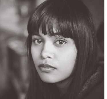 Indoor image of serene Asian, Indian young woman at home  She is sitting in kitchen at day time and looking at camera with blank expression  One person, head shot and selective focus with copy space 